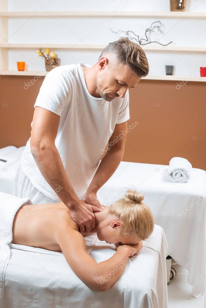 handsome masseur doing neck massage to blonde woman 