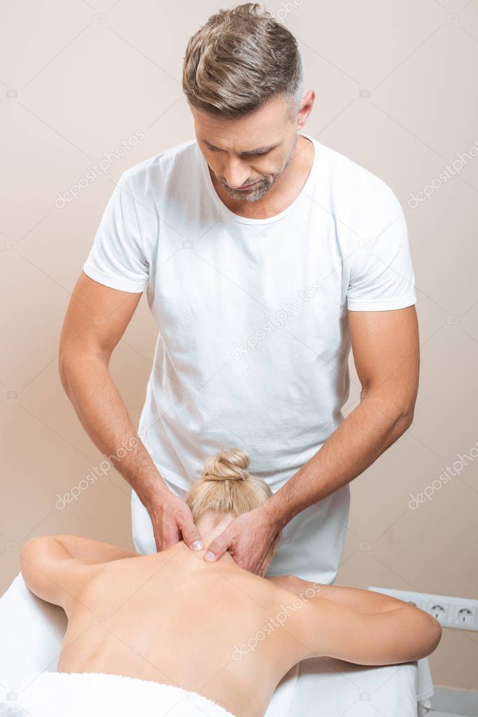 handsome masseur doing neck massage to woman in spa