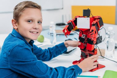 Çocuk holding kırmızı elektrikli robot gülümseyen ve kök ders sırasında kameraya bakıyor