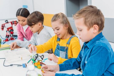 concentrated children sitting at desk and making robots in stem education class clipart