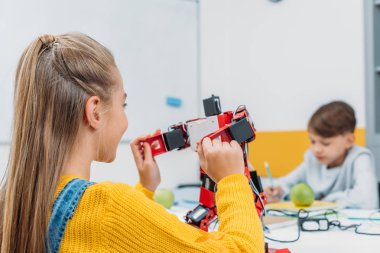 masada oturan ve zemin üzerine sınıf arkadaşı ile kök ders sırasında robot modeli tutan kız öğrenci