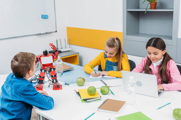 schoolchildren writing and using laptop at STEM robotics lesson