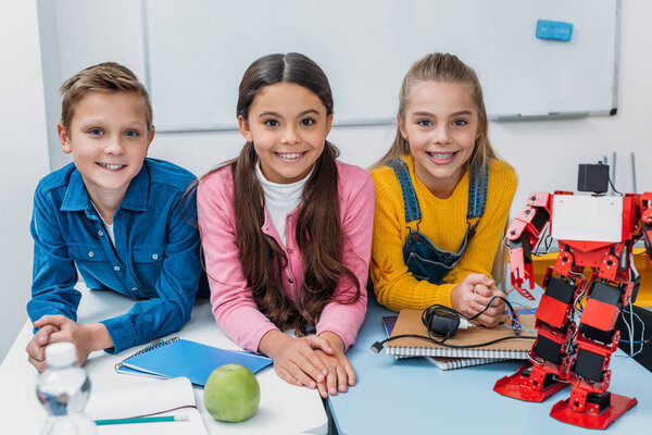 preteen schoolchildren sitting at desk, smiling and looking at camera in stem class