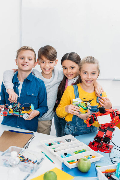 happy schoolchildren looking at camera and holding handmade robots in stem class