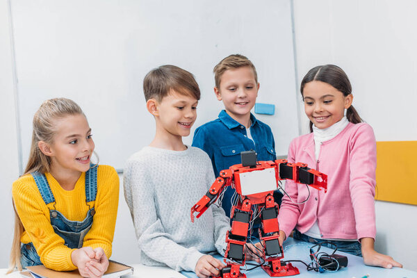 smiling schoolchildren looking at red robot handmade on desk in stem class