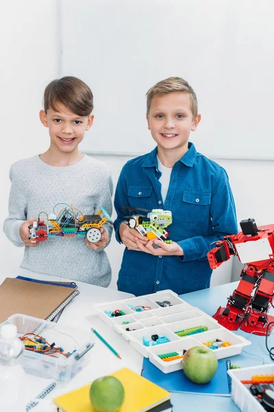 Lächelnde Schüler Blicken Die Kamera Und Halten Elektroroboter Klassenzimmer — kostenloses Stockfoto