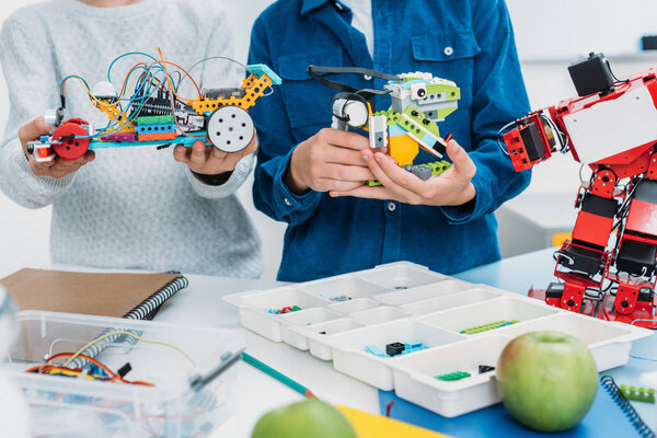 cropped view of schoolboys holding handmade robots in stem class