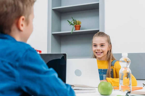 Χαμογελώντας Μαθήτρια Και Μαθητής Κάθεται Στο Γραφείο Χρησιμοποιούν Φορητούς Υπολογιστές — Δωρεάν Φωτογραφία