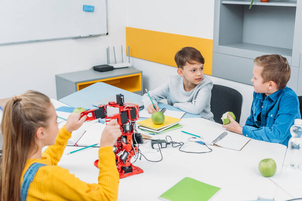 schoolchildren programming robot together and eating apples during STEM educational class