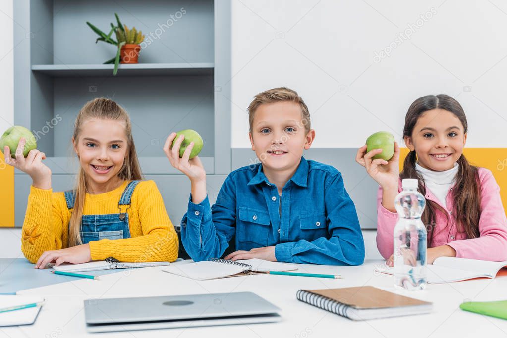 cheerful classmates rejoicing with green apples in hands after lesson