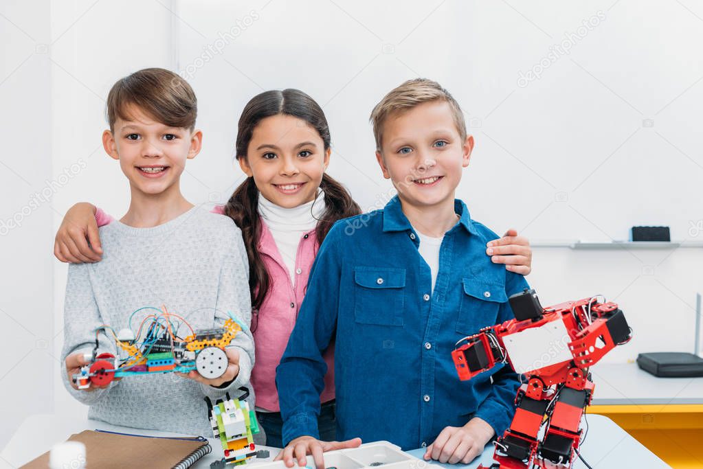 happy schoolchildren holding electric robot and looking at camera in stem class
