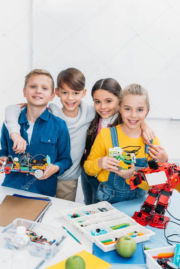 happy schoolchildren looking at camera and holding handmade robots in stem class