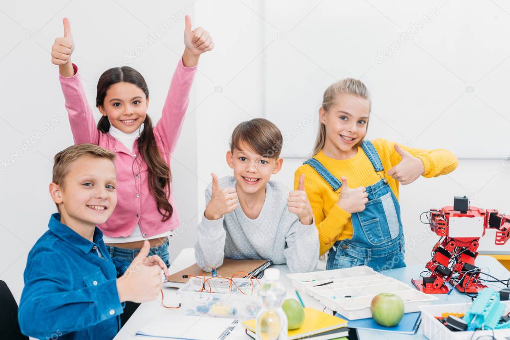 cheerful schoolchildren looking at camera and showing thumbs up while having STEM lesson