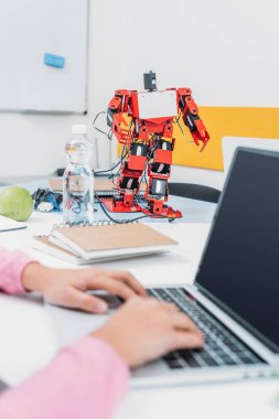 robot modeli ile masada oturan ve dizüstü bilgisayar ile boş ekran kullanarak kök ders sırasında kız öğrenci kırpılmış görünümünü  