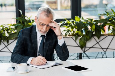 İşyerinde oturan ve not defterinde yazılı odaklanmış olgun iş adamı