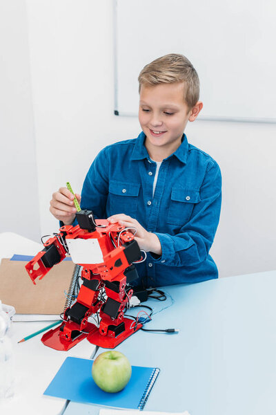 happy schoolboy working on handmade robot model during STEM lesson  