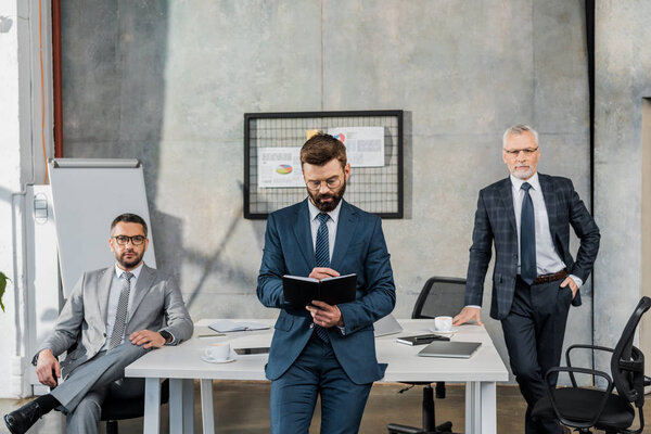 three professional bearded businessmen in suits and eyeglasses working together in office