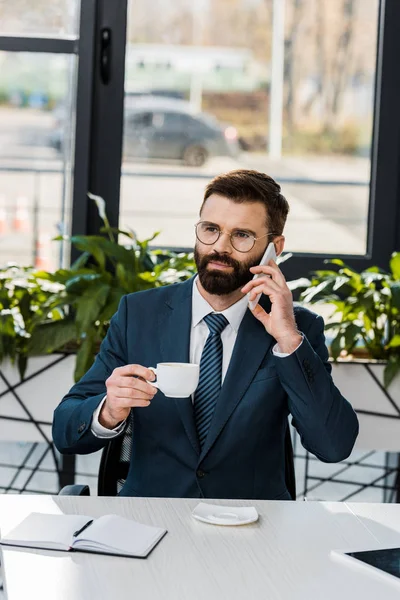 Serious Bearded Businessman Holding Cup Coffee Talking Smartphone Office — Free Stock Photo