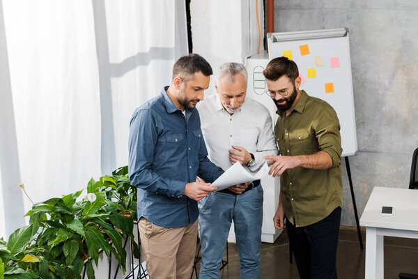 three professional businessmen discussing blueprint in office