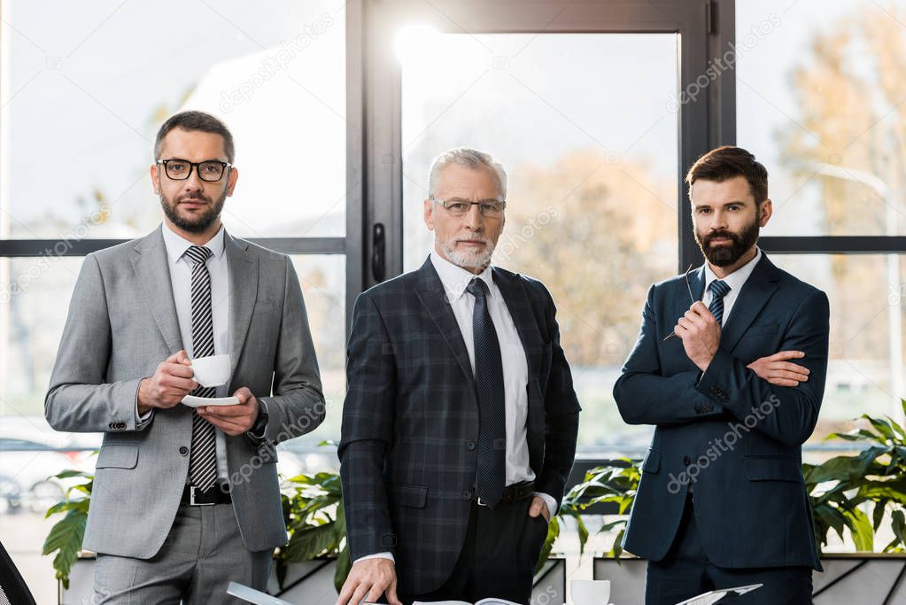 handsome businessmen in suits standing and looking at camera in office