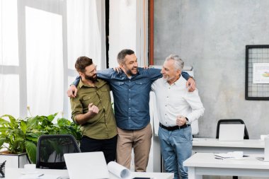 three smiling handsome businessmen hugging and standing in office