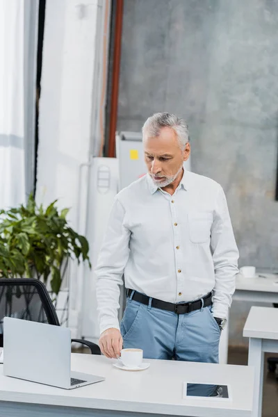 Συλλογισμένος Όμορφος Μέσης Ηλικίας Επιχειρηματίας Στέκεται Και Κοιτάζοντας Φορητό Υπολογιστή — Φωτογραφία Αρχείου