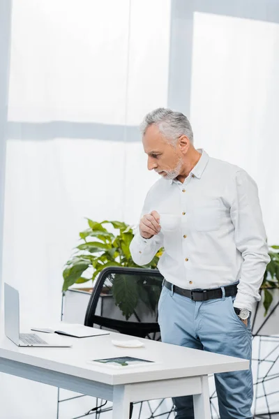 Guapo Hombre Negocios Mediana Edad Sosteniendo Taza Mirando Computadora Portátil — Foto de stock gratis