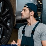 Zijaanzicht van geconcentreerde reparateur met Kladblok controleren auto wielen op de auto reparatiewerkplaats