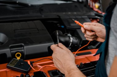 cropped shot of auto mechanic with multimeter voltmeter checking car battery voltage at mechanic shop clipart