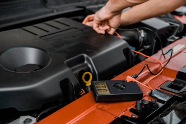 partial view of auto mechanic with multimeter voltmeter checking car battery voltage at mechanic shop clipart