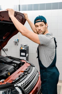 auto mechanic looking away examining car cowl at workshop clipart