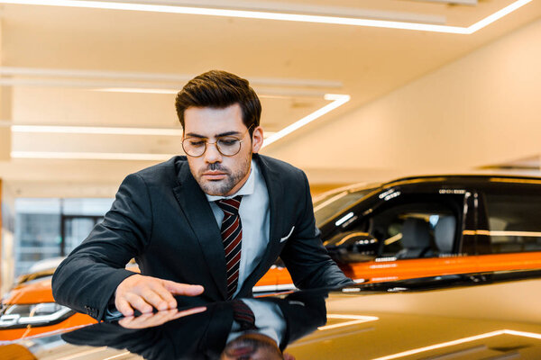young focused businessman in eyeglasses choosing automobile in dealership salon