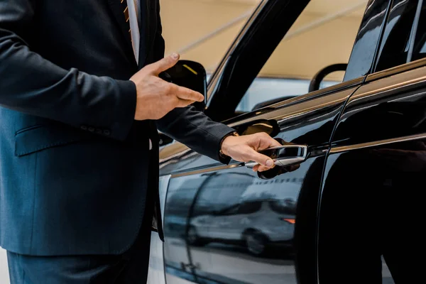 Imagen Recortada Concesionario Automóviles Masculinos Abriendo Puerta Apuntando Automóvil Negro —  Fotos de Stock