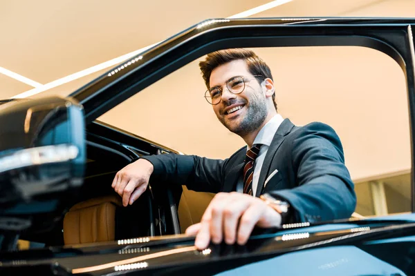 Nízký Úhel Pohled Šťastný Podnikatel Brýlích Pózuje Automobilu Autosalonu — Stock fotografie