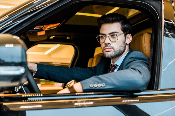 young stylish businessman in eyeglasses sitting in luxury car