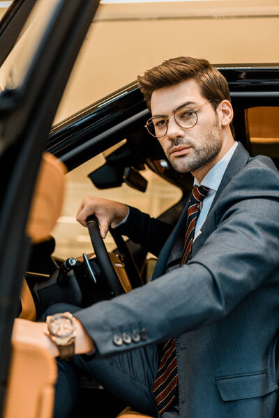 serious businessman closing door while sitting in automobile