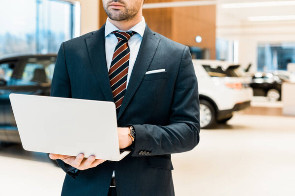 partial view of businessman in formal suit using laptop at dealership salon