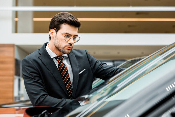 businessman in eyeglasses choosing car in dealership salon