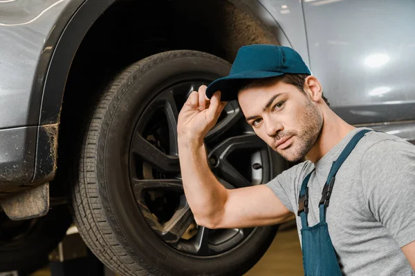 在修理店的男性汽车修理工在工作整体摆姿势附近汽车的画像 — 图库照片