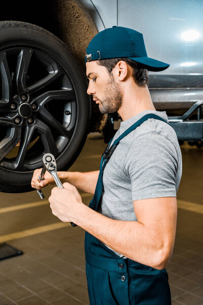 side view of male auto mechanic in working overall standing with wheel wrench at auto mechanic shop