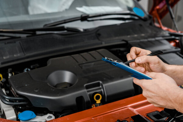 cropped shot of repairman with notepad examining car at auto repair shop