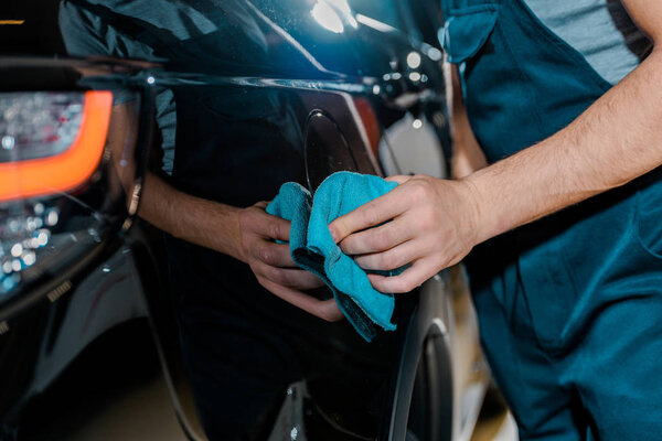 cropped shot of auto mechanic cleaning car with rag at auto repair shop