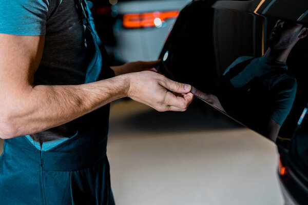 cropped shot of auto mechanic checking car trunk at auto repair shop