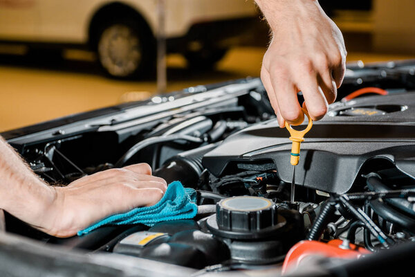 cropped shot of auto mechanic with rag checking automobile