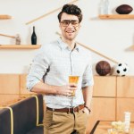 Retrato de homem sorridente em óculos com copo de cerveja na mão no café