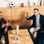 Blick aus der Vogelperspektive auf ein lächelndes multiethnisches Business-Team mit Bier, das gemeinsam im Café ruht