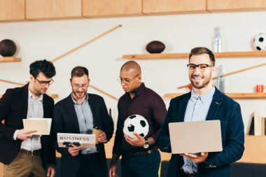 kafede çok kültürlü meslektaşları ile kameraya bakarak dizüstü bilgisayar ile gülümseyen iş adamı