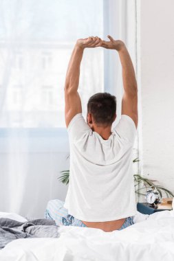 rear view of man stretching in morning in bedroom clipart