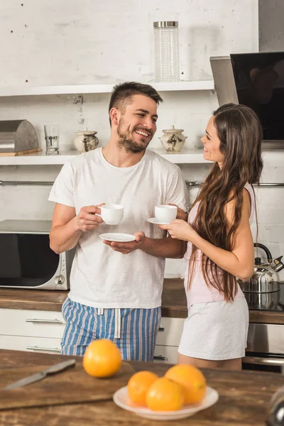 ガール フレンドとコーヒーのカップを保持しているとキッチンで朝のお互いを見て彼氏の笑顔 — ストック写真