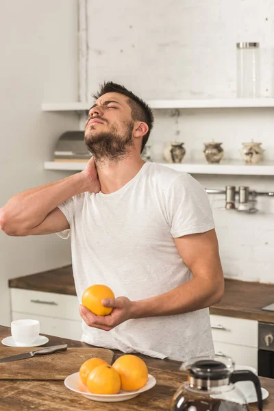 Handsome Man Holding Orange Touching Neck Morning Kitchen — Free Stock Photo